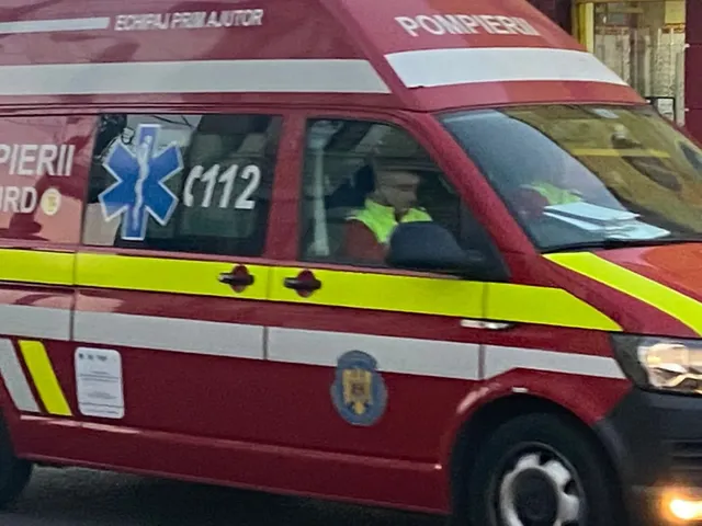 Un vehicul de serviciu de culoare roșie cu marcaje galbene și inscripții de ajutor medical este parcat pe o stradă.