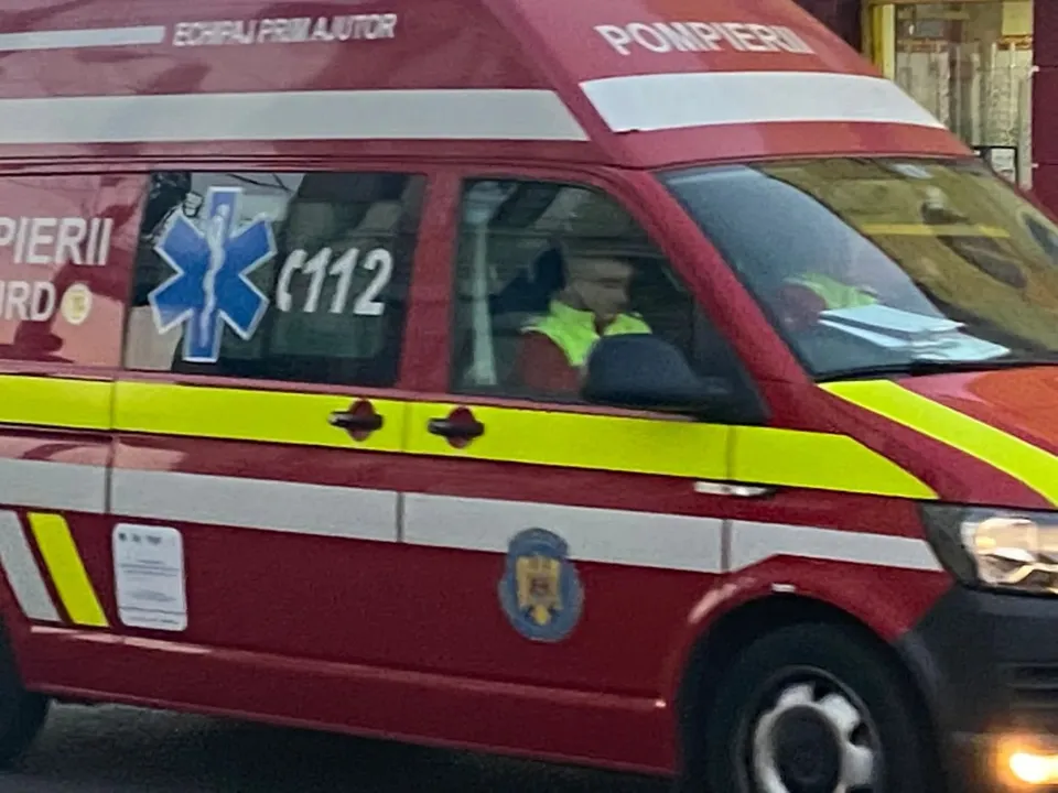 Un vehicul de serviciu de culoare roșie cu marcaje galbene și inscripții de ajutor medical este parcat pe o stradă.