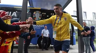 Un bărbat într-un tricou galben și pantaloni scurți de sport se întinde spre mai mulți oameni de pe partea stângă a imaginii.