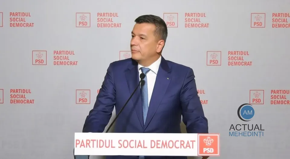 Un bărbat cu păr scurt, purtând sacou albastru și cravată albastră, stă în fața unui fundal cu logourile Partidului Social Democrat.