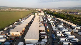 O vedere aeriană prezintă rânduri de pavilioane lungi și albe dispuse paralel, flancate de numeroase vehicule albe parcate pe ambele părți.
