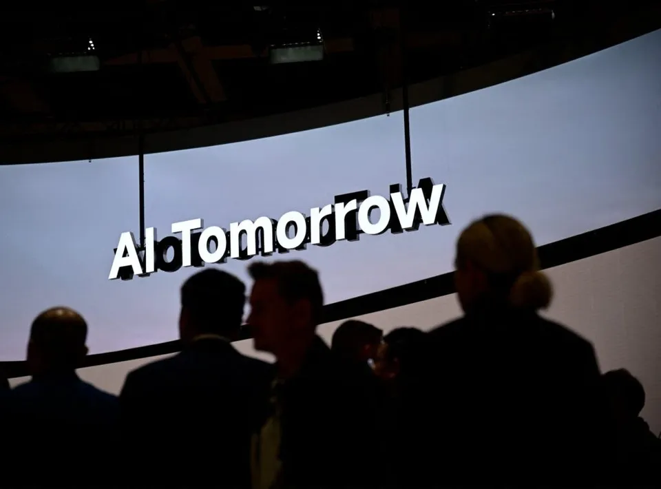 Siluetele unor persoane stau în fața unui ecran mare pe care scrie textul alb AI Tomorrow.