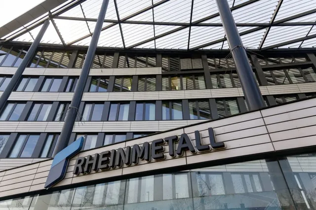 Un clădire modernă cu fațadă din sticlă și panouri metalice prezintă un logo cu textul RHEINMETALL sub o structură de acoperiș metalică.