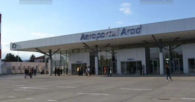 O clădire de terminal cu inscripția Aeroportul Arad, sub un acoperiș plat, cu persoane stând pe o suprafață asfaltată în față.