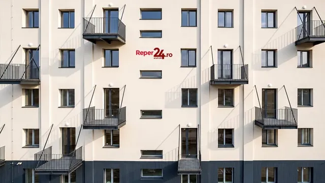 O clădire de apartamente cu fațadă albă și gri prezintă ferestre rectangulare și balcoane negre cu balustrade metalice.