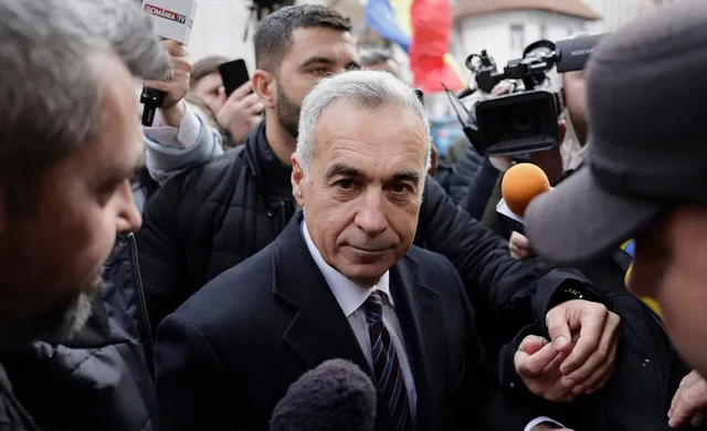 Un bărbat cu părul cărunt și costum întunecat este înconjurat de persoane care țin microfoane și telefoane mobile în apropierea feței sale.