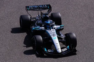 Un monopost de Formula 1 de culoare închisă cu accente albastre și verzi circulă pe o pistă de asfalt gri.
