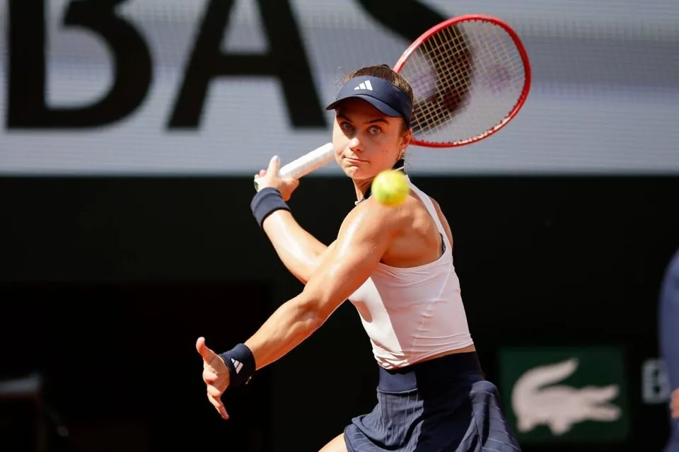 O femeie cu o șapcă neagră și o cană albă ține o raketă de tenis în timp ce o minge galbenă zboară în fața ei.