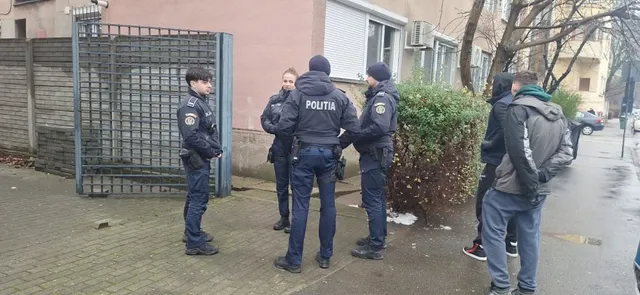 Patru polițiști în uniformă și trei civili stau pe un trotuar lângă un gard metalic și un tufiș verde.