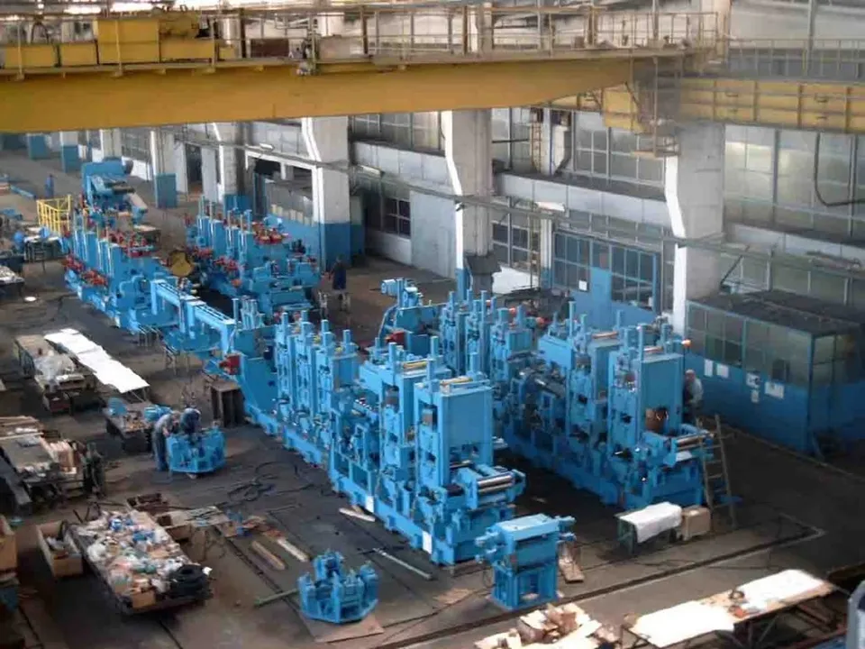 Linii de producție industriale de culoare albastră sunt amplasate pe un podea de fabrică mare, înconjurate de diverse utilaje și materiale.