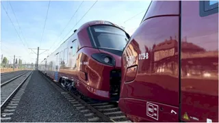 Două rame electrice de culoare roșie sunt oprite pe șine lângă un sector de balast sub un cer senin.