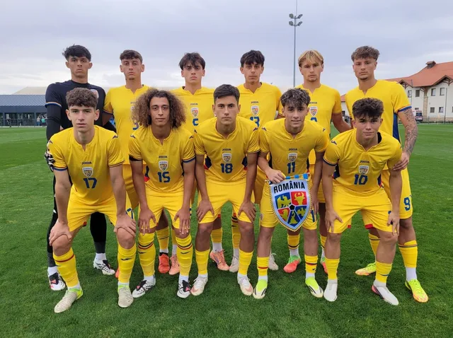 O echipă de nouă sportivi îmbrăcați în echipamente galbene și negre stă în rânduri pe un teren de fotbal sub un cer înnorat.