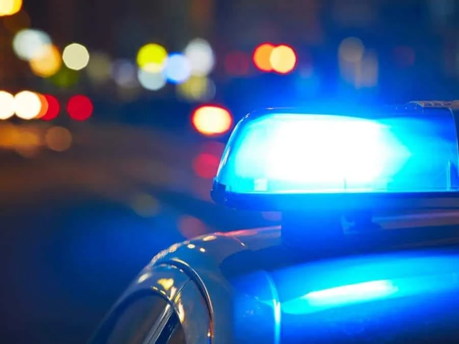 O lumină albastră de avertizare este montată pe acoperișul unui vehicul, cu lumini colorate difuze în fundalul nocturn.