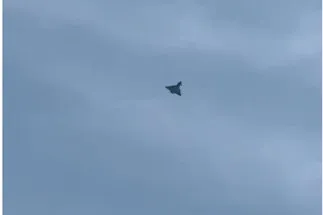 O siluetă întunecată de avion zboară pe un cer acoperit de nori gri.