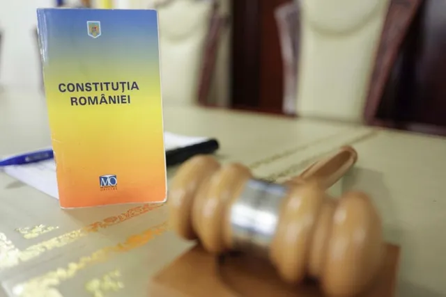 O carte cu textul Constituția României stă pe o masă lângă un ciocan de lemn.