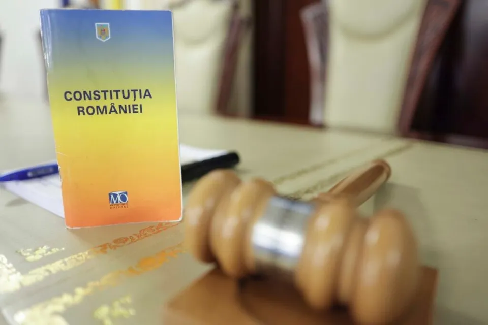 O carte cu textul Constituția României stă pe o masă lângă un ciocan de lemn.