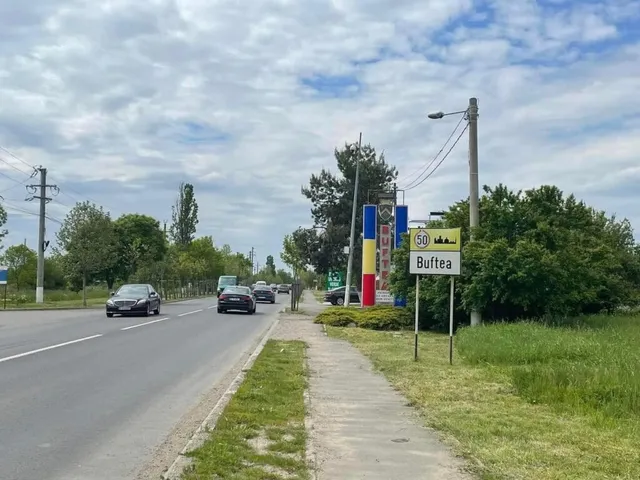 O stradă asfaltată cu mașini circulând este alături de un trotuar și un panou indicativ pe care scrie Buftea.