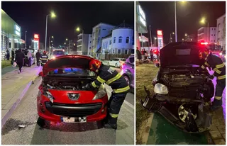 Două persoane în uniforme de protecție cu benzi reflectorizante inspectează motoarele unor autoturisme avariate pe un drum urban noaptea.