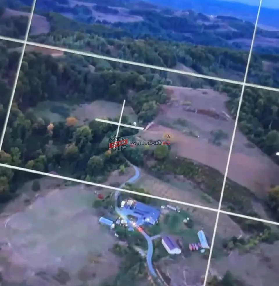 Vedere aeriană cu dealuri împădurite, poieni, câteva construcții și linii albe suprapuse.