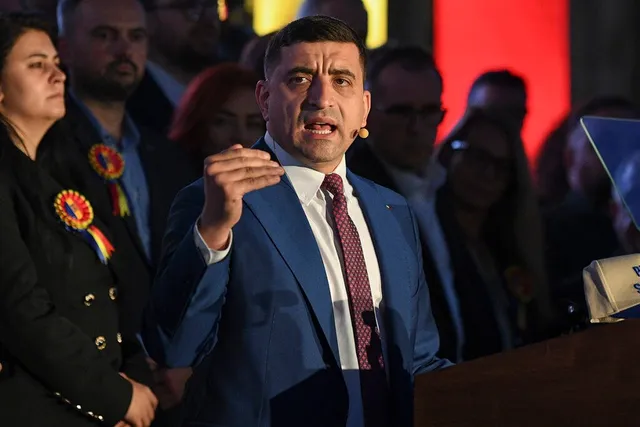 Un bărbat într-un costum albastru și cravată roșie vorbește în fața unui grup de persoane din spatele unui podium.
