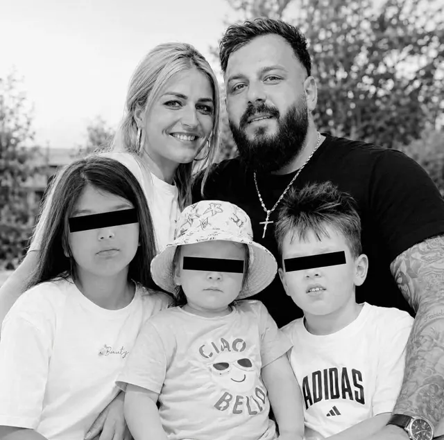 O femeie zâmbindă stă lângă un bărbat cu barbă, înconjurați de trei copii cu ochii acoperiți de benzi negre.