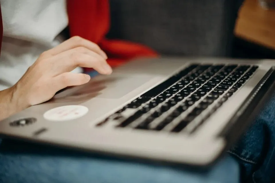O persoană folosește un laptop deschis, având mâinile plasate pe tastatură și pe zona touchpad-ului.