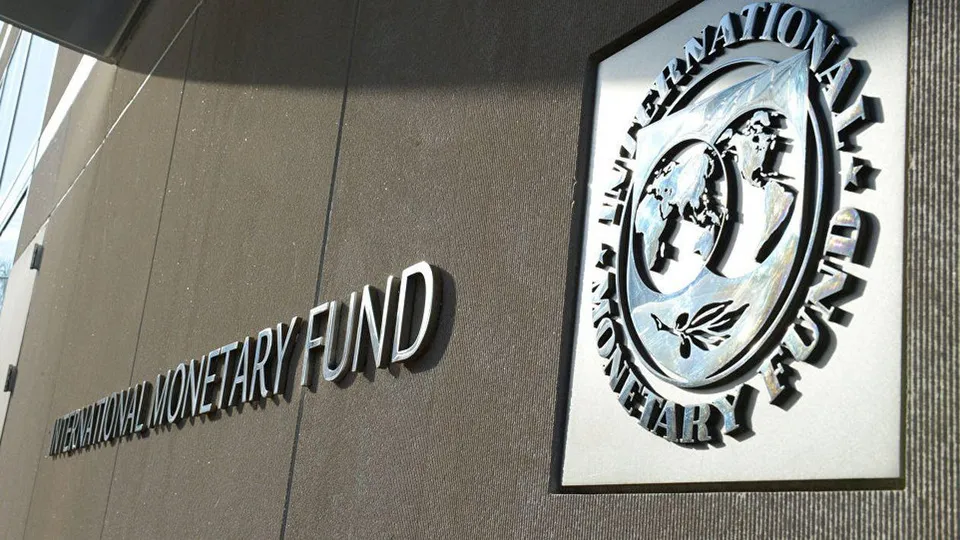 Un semn cu textul "INTERNATIONAL MONETARY FUND" și un logou circular cu o hartă a lumii sunt montate pe un perete gri.