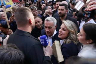 O femeie cu părul blond și un bărbat cu părul cărunt sunt înconjurați de o mulțime de oameni și microfoane.