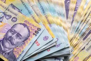 Mai multe bancnote de o sută de lei sunt întinse într-un evantai pe un fundal neutru.