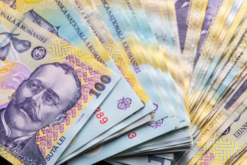 Mai multe bancnote de o sută de lei sunt întinse într-un evantai pe un fundal neutru.