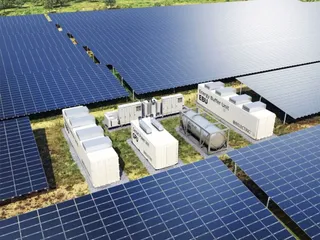 O ilustrație digitală prezintă panouri solare dispuse în rânduri și unități de stocare a energiei albe amplasate pe un teren cu iarbă.