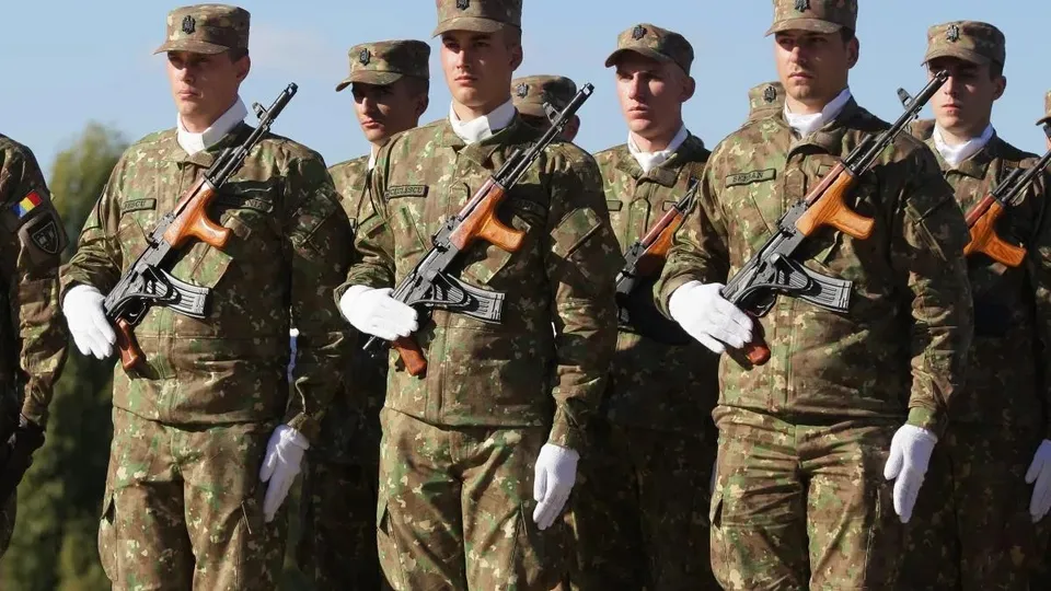 Cinci soldați în uniformă de camuflaj portțin militari și mănuși albe, stând în rând sub un cer senin.
