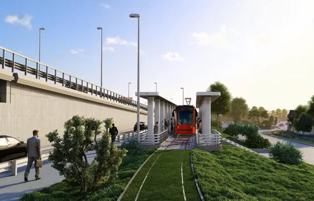 Un tramvai roșu circulă pe o linie de tren lângă o stație cu acoperiș, în timp ce un bărbat merge pe un trotuar lângă vegetație.