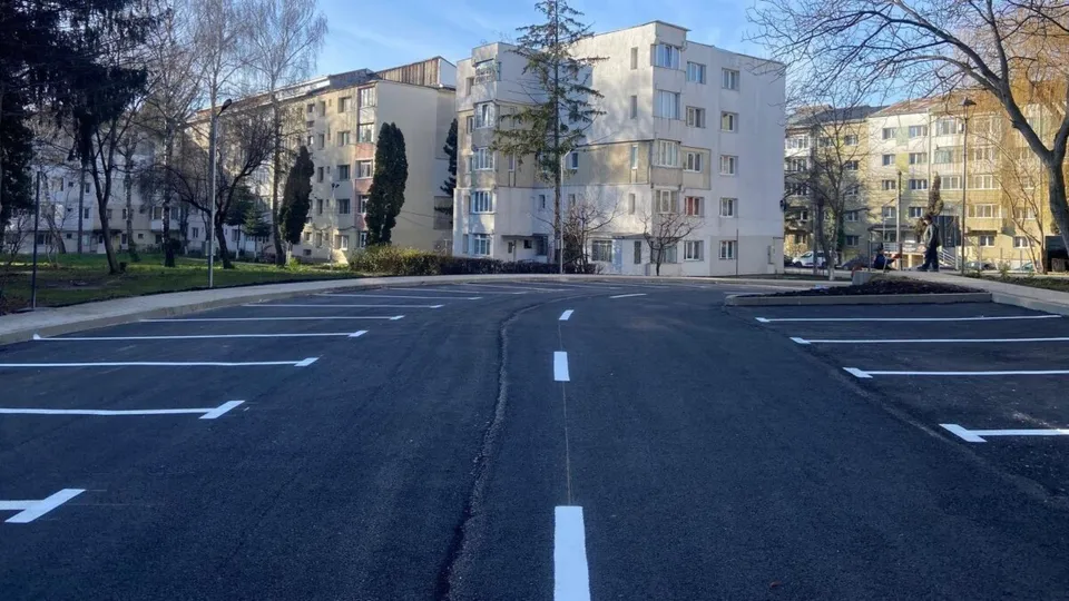 O parcare proaspăt asfaltată cu locuri marcate cu linii albe, în fața unor blocuri de locuințe într-un cartier urban.