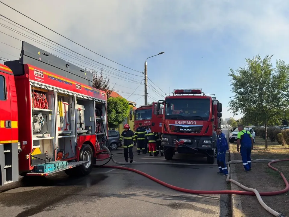 Mai multe autospeciale de pompieri roșii sunt parcate pe un drum, cu echipamente deschise și furtunuri întinse pe asfalt.