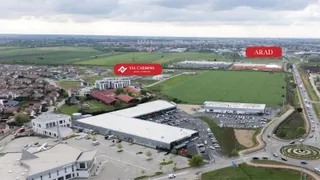 O vedere aeriană prezintă clădiri comerciale, terenuri verzi, parcuri de staționare cu mașini și o stradă cu trafic lângă un sens giratoriu.