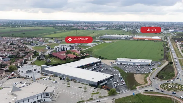 O vedere aeriană prezintă clădiri comerciale, terenuri verzi, parcuri de staționare cu mașini și o stradă cu trafic lângă un sens giratoriu.