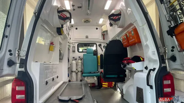 Interiorul unei ambulanțe cu uși deschise, echipată cu o butelie de oxigen, un scaun de culoare turcoaz și un pat de transport metalic.