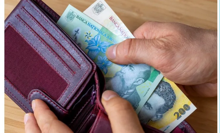 O persoană ține un portofel deschis de culoare purpurie din care scoate câteva bancnote de 200 de lei.