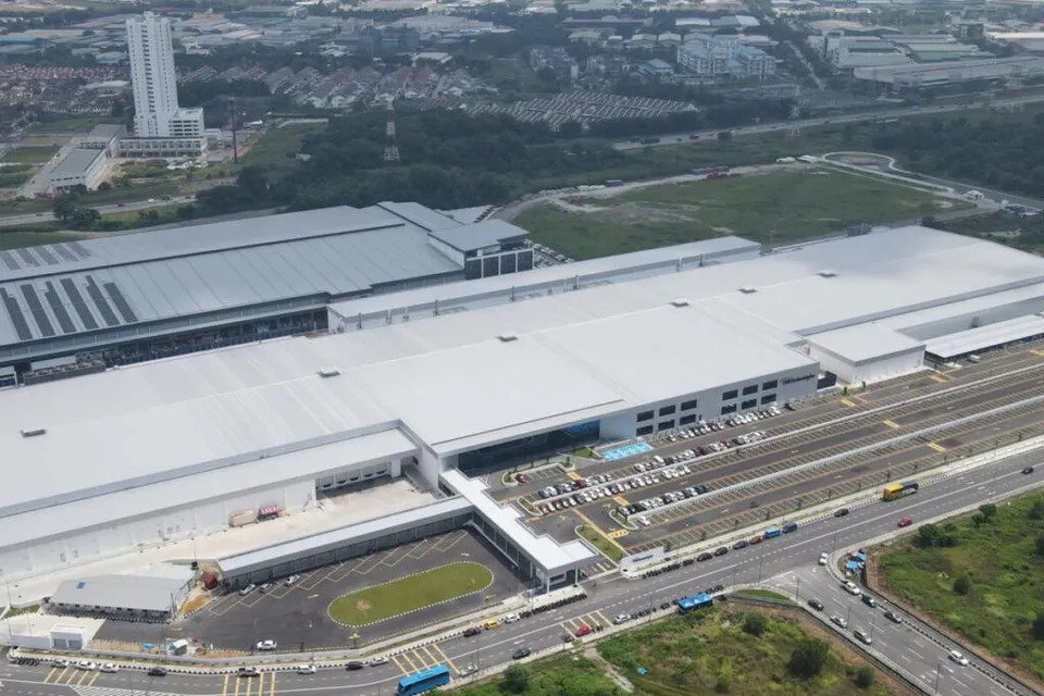 O vedere aeriană prezintă un complex industrial de mari dimensiuni cu acoperișuri plate și gri, situat lângă o autostradă și o zonă de parcare.