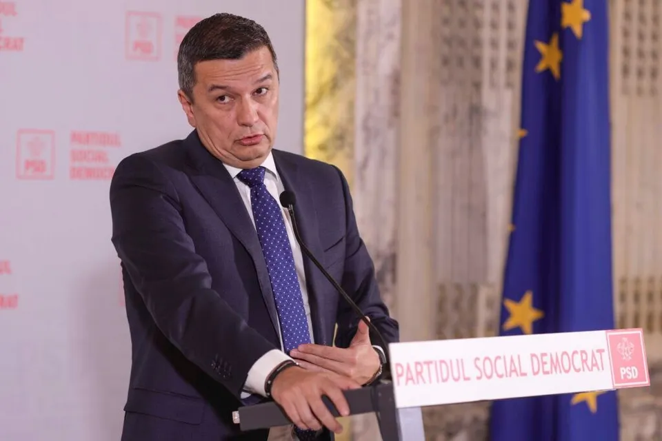 Un bărbat într-un costum închis la culoare și cravată albastră stă în spatele unui podium cu inscripția Partidul Social Democrat.