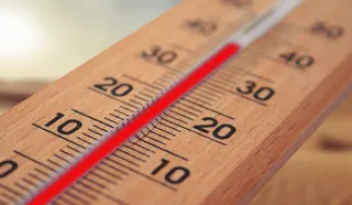 Un termometru analogic cu cadru din lemn prezintă o coloană de lichid roșu situată între marcajele de douăzeci și treizeci de grade.