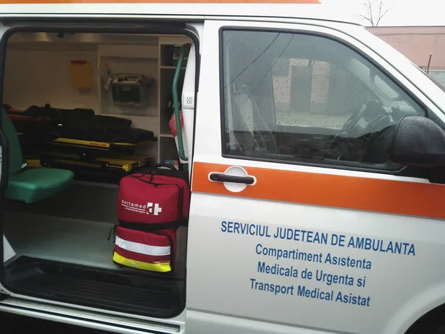 Interiorul unei ambulanțe cu echipamente medicale și o geantă roșie de transport aflată lângă scaunul verde.