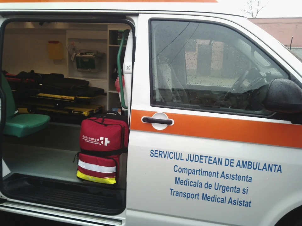 Interiorul unei ambulanțe cu echipamente medicale și o geantă roșie de transport aflată lângă scaunul verde.