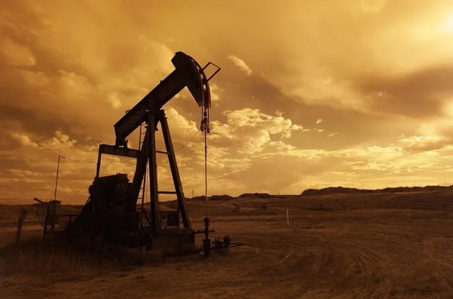 O pompa de petrol este siluetată în fața unui cer gălbui sub un apus sau răsărit.