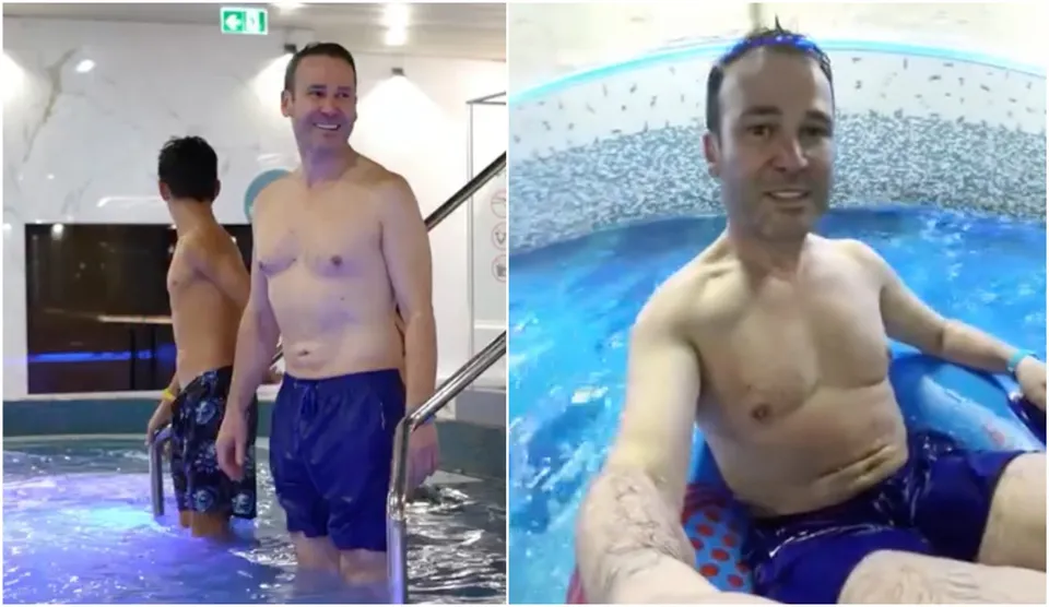Un bărbat cu șort albastru stă într-o piscină, în timp ce un alt bărbat cu șort în culori închise se află în spatele lui lângă scări metalice.