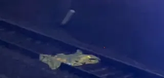 O siluetă umană este întinsă pe o suprafață întunecată lângă o structură metalică sub un cer de noapte.