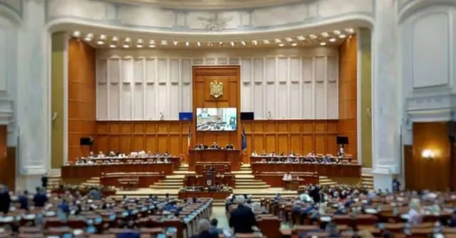 Sală parlamentară cu tribune, pupitre, ecrane, steme și numeroși oameni așezați în plan frontal și central.