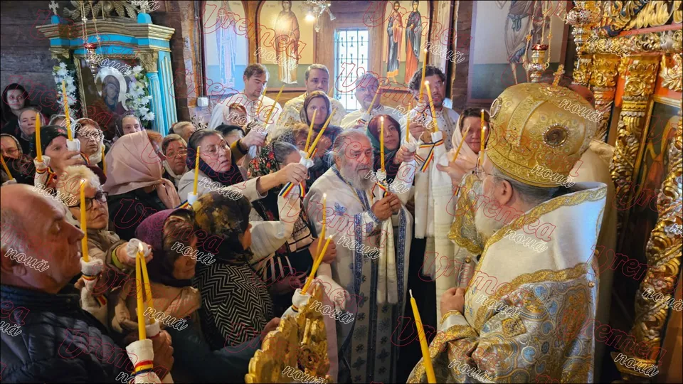 Un grup de persoane ține lumânări aprinse în interiorul unei biserici, în fața unui cleric îmbrăcat în haine liturgice aurii și al un another cu mitră.