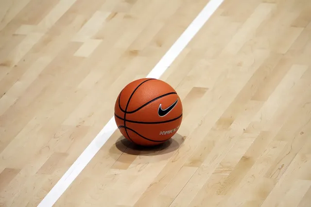 Un rând de linii albe desparte un teren de baschet din lemn pe care se află o minge portocalie cu logo-ul Nike.